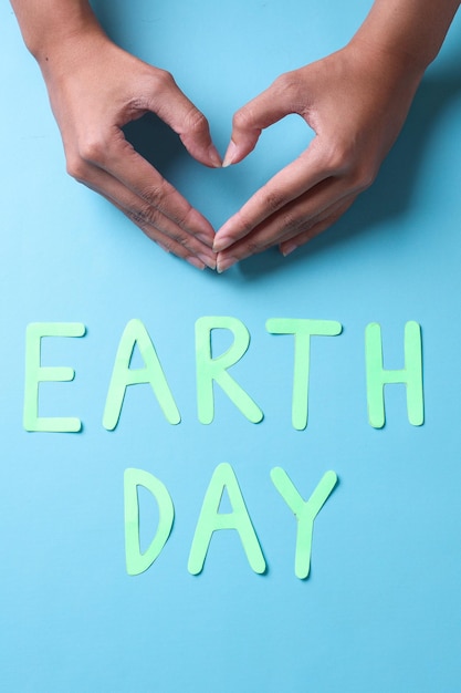 earth day words and fingers forming heart shape on blue background. World earth day concept.