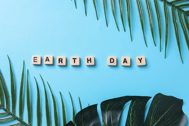 слова день земли и различные зеленые листья, изолированные на синем фоне. Концепция Всемирного дня земли.