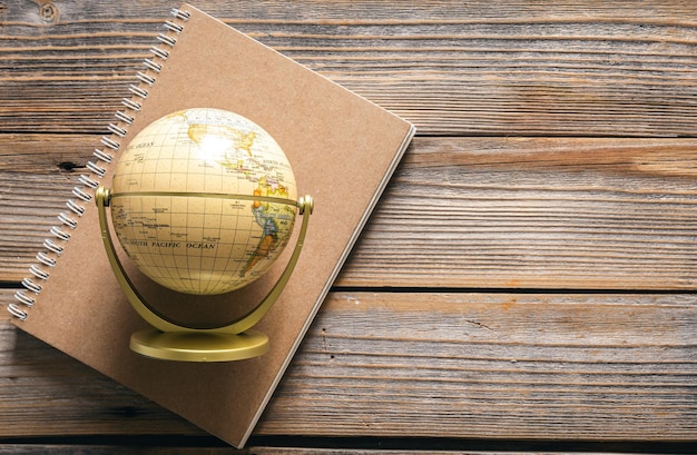 Earth globe and notebook on wooden background top view