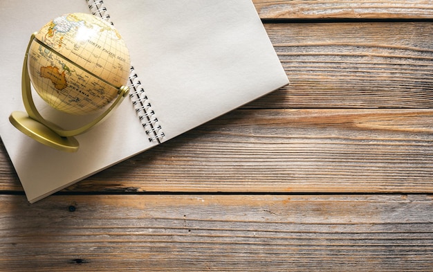 Earth globe and notebook on wooden background top view