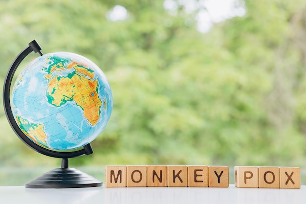 Earth globe and wooden cube with the word MONKEY POX on green background