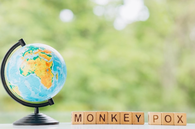 Earth globe and wooden cube with the word MONKEY POX on green background