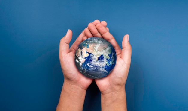 Photo earth in hands. world, small globe hold and supported by human hand with love and care, on blue background. earth day. save the planet. energy saving concept. elements of this image furnished by nasa.