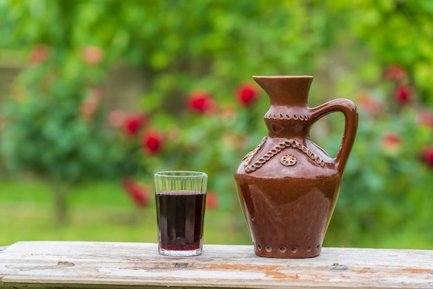 Brocca di terracotta e bicchiere di vino rosso sullo sfondo del giardino estivo su un tavolo di legno, primo piano