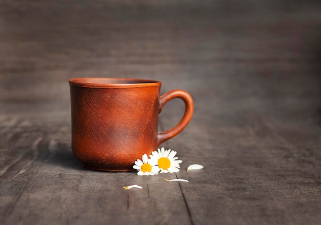 黒の背景にカモミールの花のクローズアップと陶器のマグカップ