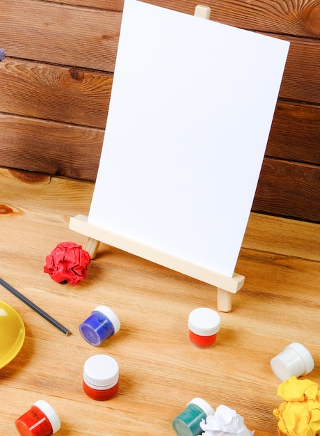 Easel, art brushes and coffee on a wooden table. Workplace of the artist. Creativity and hobby concept.