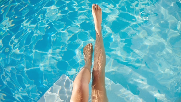 夏の足を楽にする最初のプールの水の中の女性の足のトリミングされたショット
