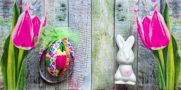 Easter background with bunny, egg and pink tulips on wooden texture. Banner format.