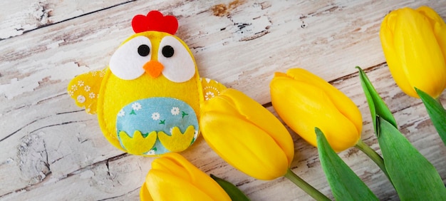 Sfondo di pasqua con pollo decorativo nel nido e tulipani gialli su sfondo di legno