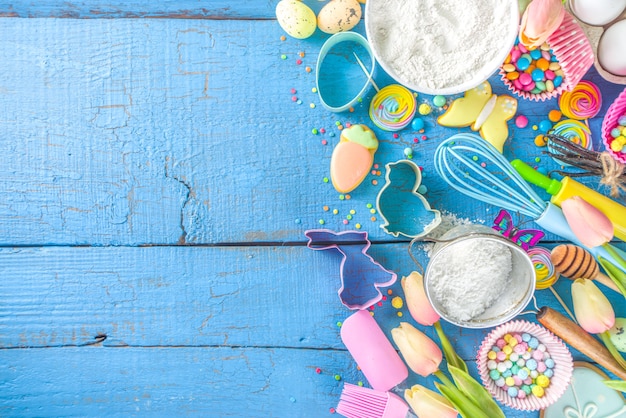 Sfondo di cottura di pasqua con mattarello, frusta, uova, farina e coriandoli di zucchero colorati