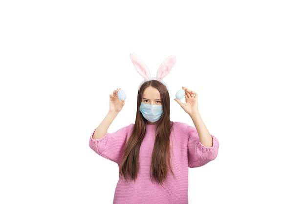 Easter banner Happy girl in bunny ears and medical mask with decorated eggs smiling isolated on a blue background in studio