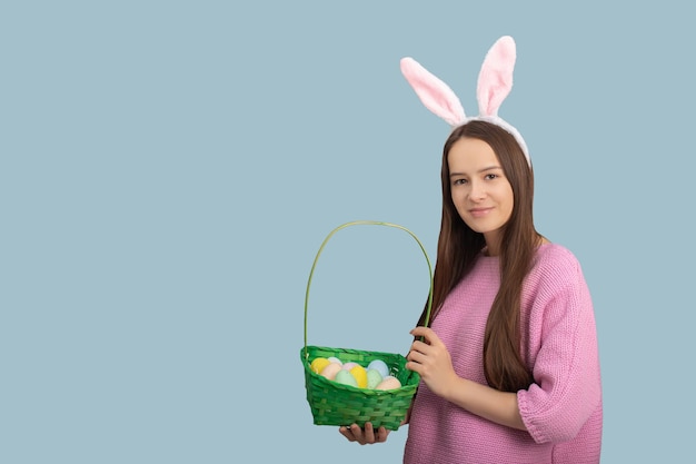 Пасхальный баннер Счастливая девушка в кроличьих ушах с корзиной украшенных яиц улыбается изолированно на синем фоне в студии