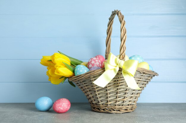 カラフルな卵と木製の背景の花でいっぱいのイースターバスケット