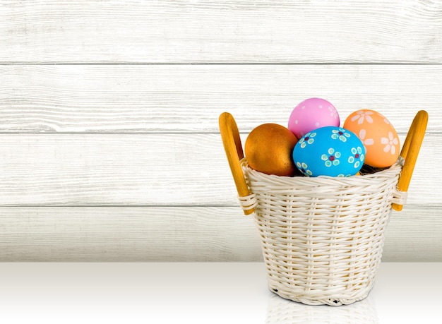Пасхальная корзина с разноцветными яйцами на белом фоне