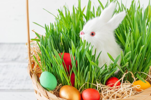 Easter basket with green grass filled with brightly colored Easter eggs and White little bunny. Happy Easter.