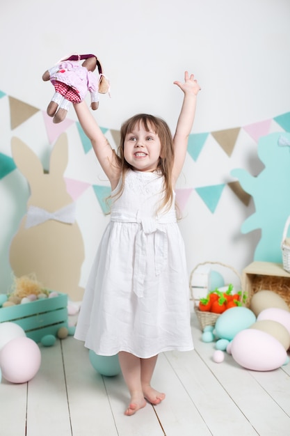Пасхальный! Красивая маленькая девочка в белом платье радуется празднику. Много различных красочных пасхальных яиц, красочный интерьер пасхи. семейный отдых. Пасхальный заяц. ребенок играет с игрушкой. фермер