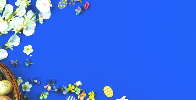 Composizione della cornice del confine di pasqua con uova e fiori dipinti a pasqua, banner con sfondo blu, vista dall'alto e foto dello spazio della copia