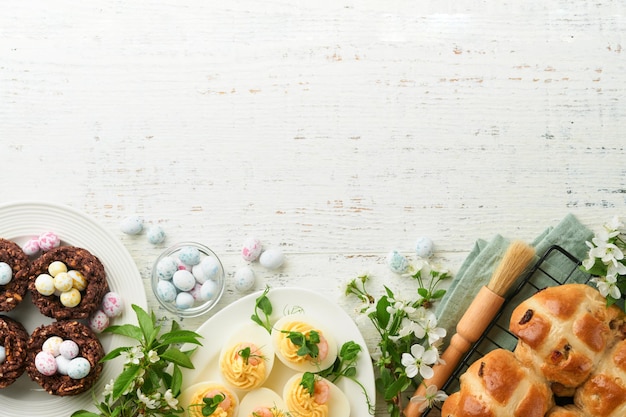 Easter brunch or breakfast Easter chocolate nest cake with chocolate candy eggs traditional hot cross buns and deviled eggs with bouquets of blooming apple trees Spring Easter holiday food concept