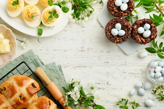 Photo easter brunch or breakfast easter chocolate nest cake with chocolate candy eggs traditional hot cross buns and deviled eggs with bouquets of blooming apple trees spring easter holiday food concept