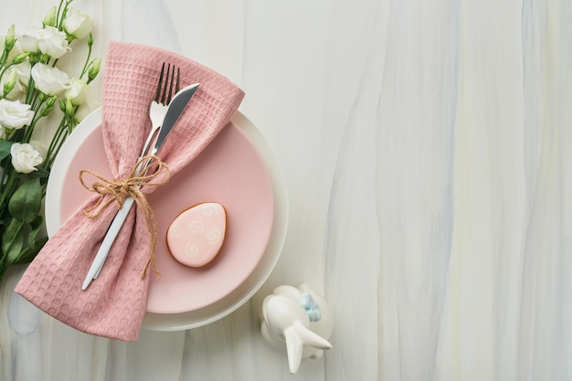 Easter brunch table setting Spring Easter holiday concept with white pink plate and napkin with decorative symbols holiday rabbit eggs and bouquet of flowers on white background Top view Mock up