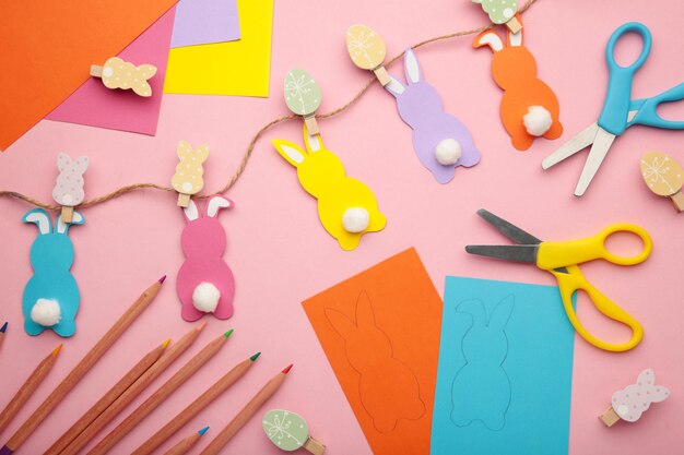 Photo easter bunnies handmade from colored paper, easy crafts for kids on pink background.