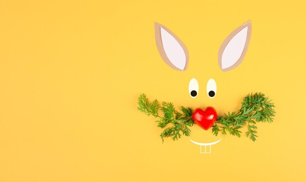 Easter bunny face with a heart shaped nose and whiskers from carrot leaves, holiday greeting card