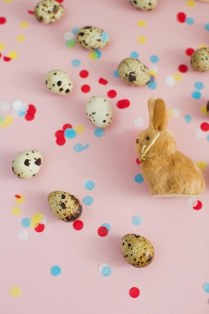 Easter bunny and quail eggs on a pink background with colorful confetti