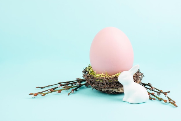 Easter bunny or rabbit sitting next to a wicker nest filled with colorful egg spring holiday