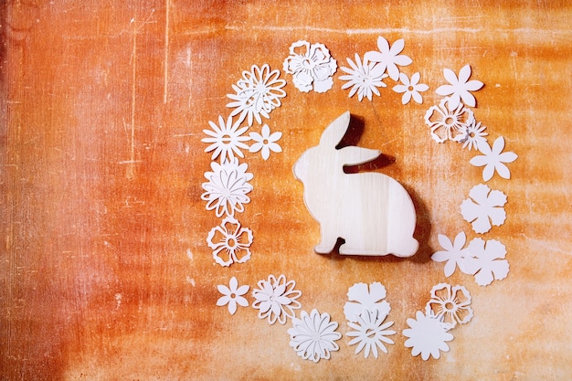 Easter bunny rabbit with different paper flowers around over orange stone wall. Flat lay, copy space. Easter holiday