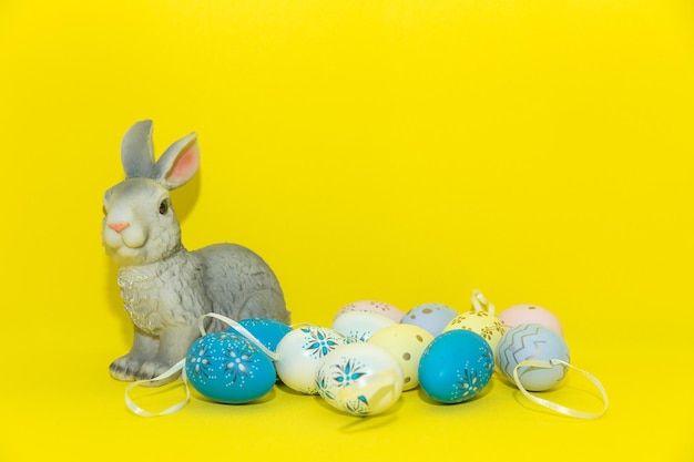 노란색 배경 부활절 휴가 개념에 고립 된 여러 가지 빛깔의 계란 사이에 앉아 부활절 토끼