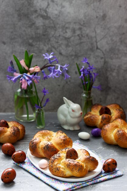 Easter buns, colored eggs and flowers on a gray concrete background.