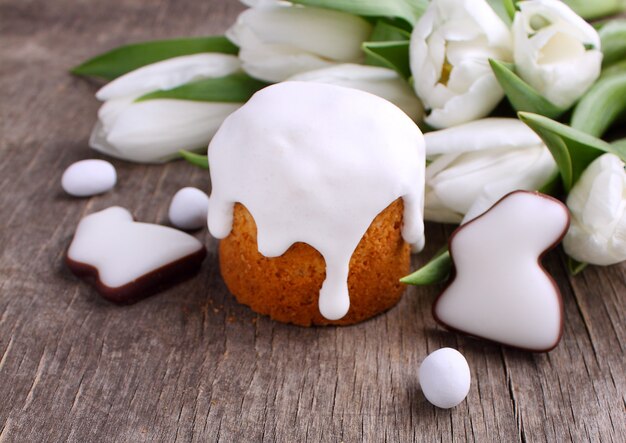 Easter cake, white tulips, chocolate bunny and eggs on a wooden background. Copy space.