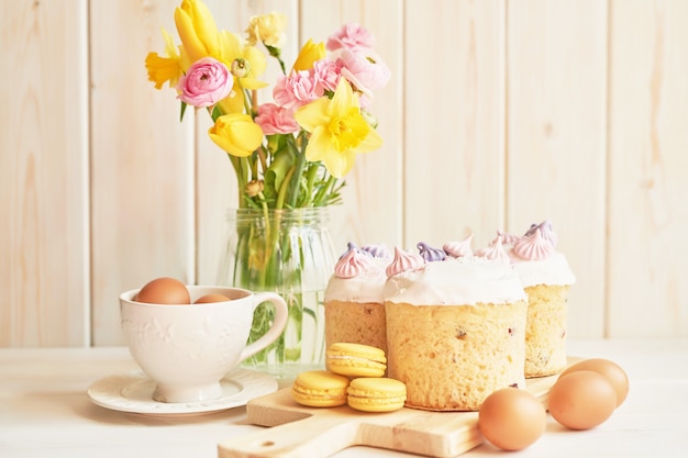 Photo easter cakes on table, macaroons, eggs and bouquet of flowers in vaseaster