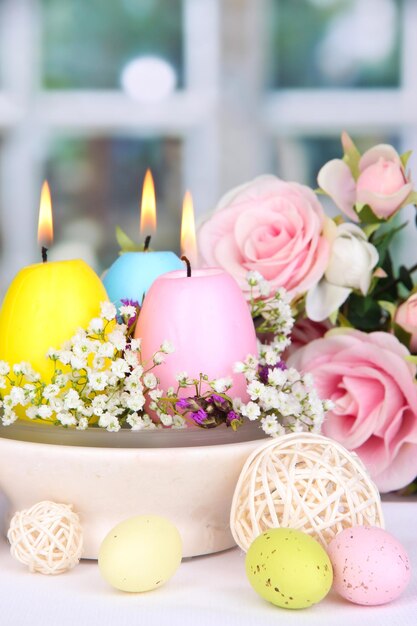 Easter candles with flowers on window background