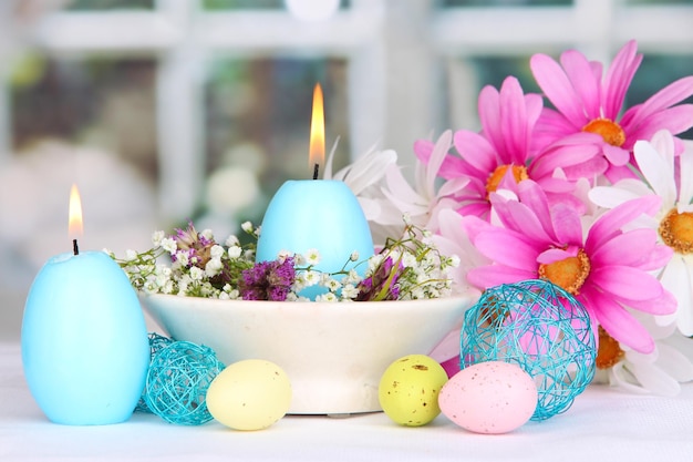 Easter candles with flowers on window background