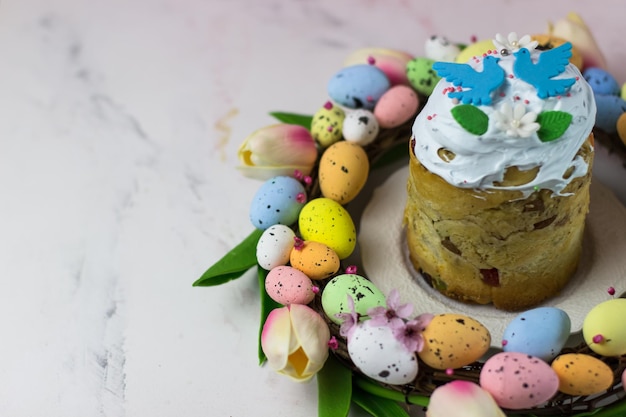 Easter card Kulich with sugar fudge in a wreath of tulips and eggs Marshmallow fudge with decoration Place for text