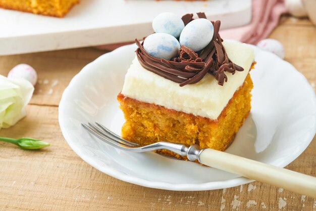 Easter carrot cake bars decorated with chocolate nest and chocolate candy eggs blossoming cherry or apple flowers on rustic light wooden backgrounds Easter holiday meal Traditional Easter food