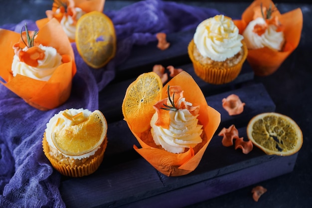 Easter carrot cupcakes with vanilla cream and caramel oranges on dark stone background