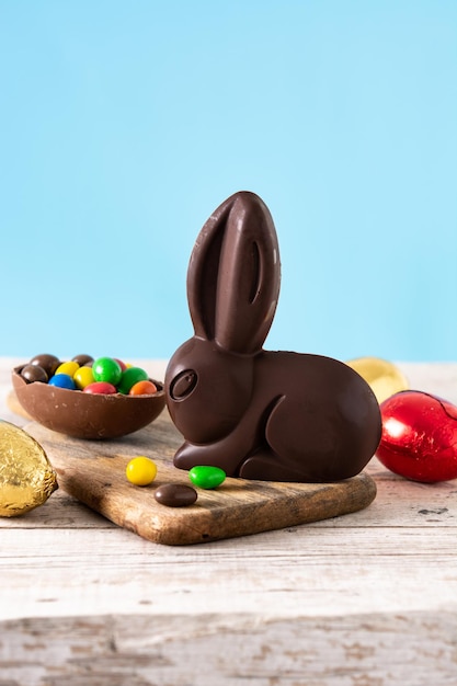 Easter chocolate bunny and colorful eggs on wooden table and blue background