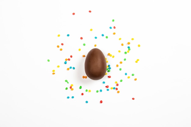 Easter chocolate egg and colorful decorations on a light surface. Easter concept, easter treats. Flat lay, top view