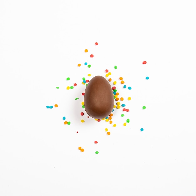 Easter chocolate egg and colorful decorations on a light surface. Easter concept, easter treats. Square. Flat lay, top view