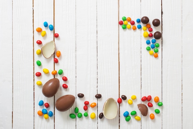 Uova di cioccolato di pasqua e caramelle su superficie di legno bianca