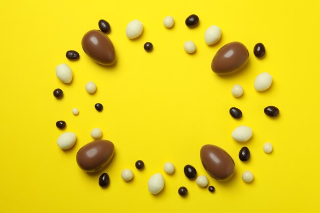 Foto uova di cioccolato di pasqua e caramelle su colore giallo