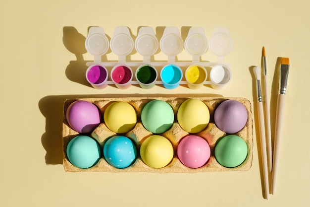 Photo easter colored multicolored eggs in a tray on a studio background next to paintbrushes and paints