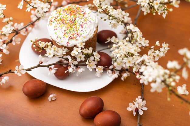 Easter composition. A blooming apricot branch, painted eggs and a glazed Easter cake decorated with sugar sprinkles.