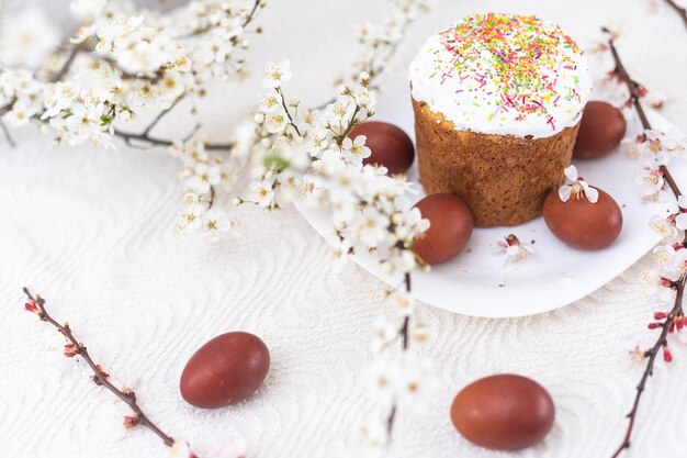 Easter composition. A blooming apricot branch, painted eggs and a glazed Easter cake decorated with sugar sprinkles.