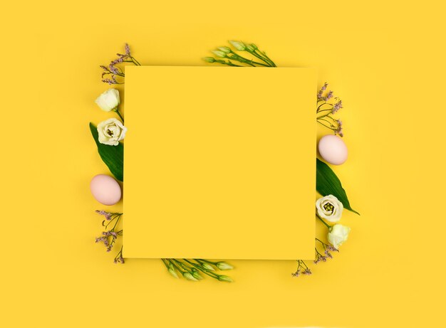 Easter composition. Easter eggs, flowers, paper blank on yellow background. 