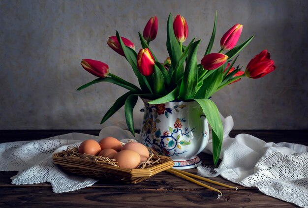 The easter composition Eggs a red tulips and church candles on wooden table closeup