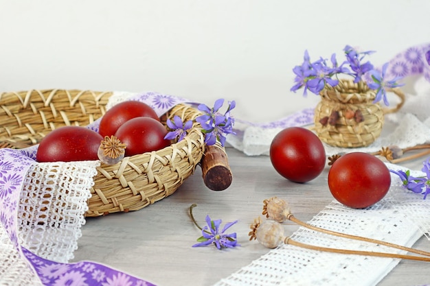 Easter composition painted eggs on a decorative tray among lace and ribbons blue flowers and poppy branches light background