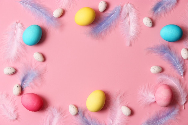 Easter composition of painted eggs and feathers on a colored background